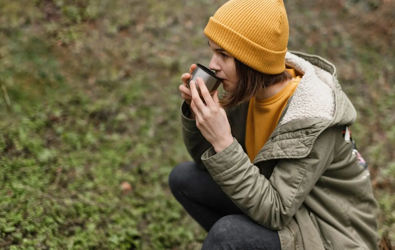 Halbnahe Aufnahme einer Frau, die im Wald Kaffee trinkt.